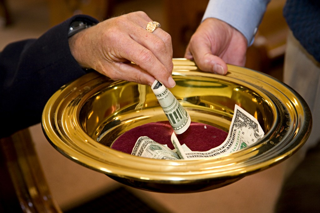 Image of a person putting money into the collection plate at church.